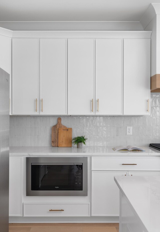 room details with stainless steel refrigerator, tasteful backsplash, white cabinetry, light countertops, and built in microwave