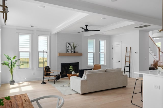 living room featuring visible vents, light wood-style floors, a brick fireplace, and beamed ceiling