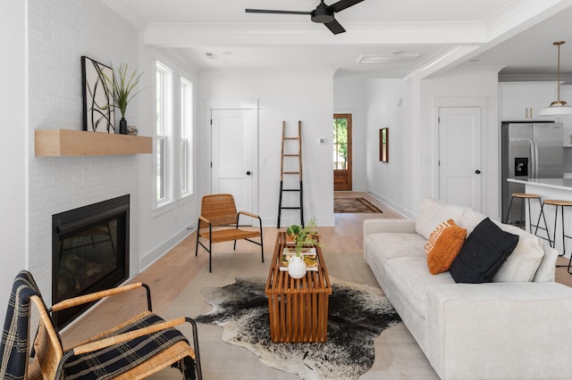 living area with ornamental molding, light wood-style floors, a fireplace, baseboards, and ceiling fan