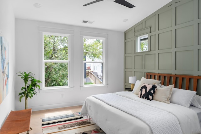 bedroom featuring visible vents, baseboards, wood finished floors, a decorative wall, and a ceiling fan