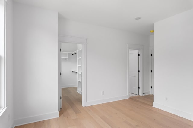 unfurnished bedroom featuring light wood-style flooring, a walk in closet, and baseboards