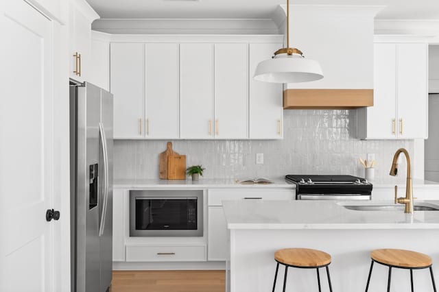 kitchen with a kitchen bar, a sink, backsplash, white cabinetry, and stainless steel appliances