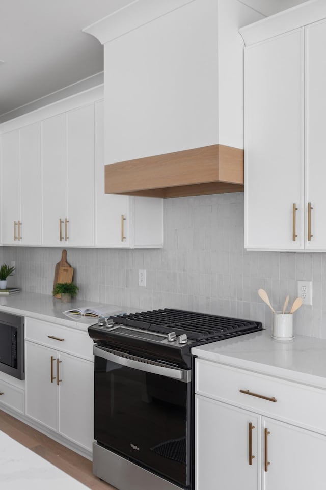 kitchen featuring stainless steel range with gas stovetop, black microwave, light countertops, and custom range hood