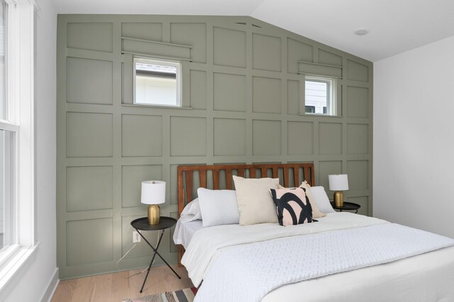 bedroom featuring multiple windows, lofted ceiling, light wood-style floors, and a decorative wall