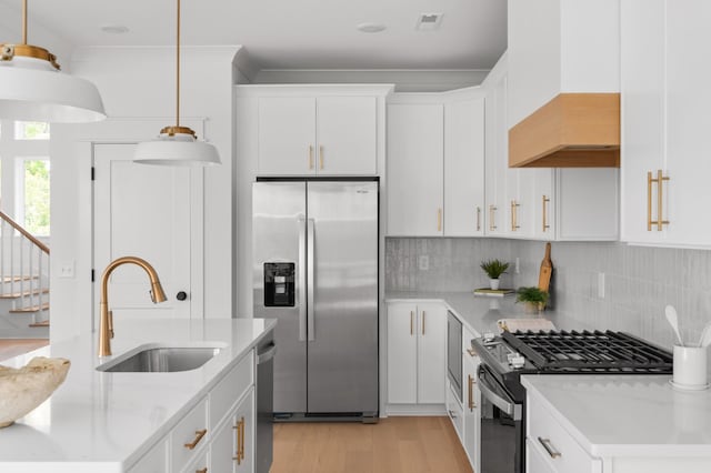 kitchen with pendant lighting, decorative backsplash, light wood-style flooring, appliances with stainless steel finishes, and a sink