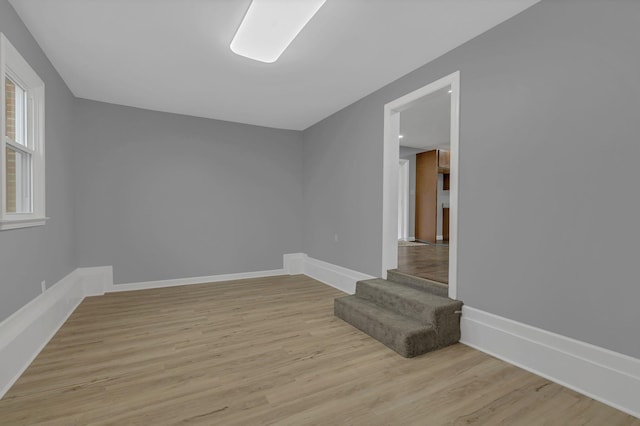 spare room featuring stairs, light wood-style floors, and baseboards