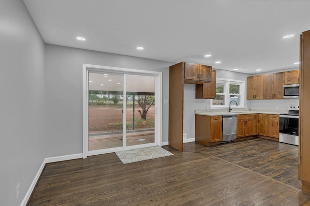 kitchen featuring light countertops, dark wood-style flooring, brown cabinets, stainless steel appliances, and a sink