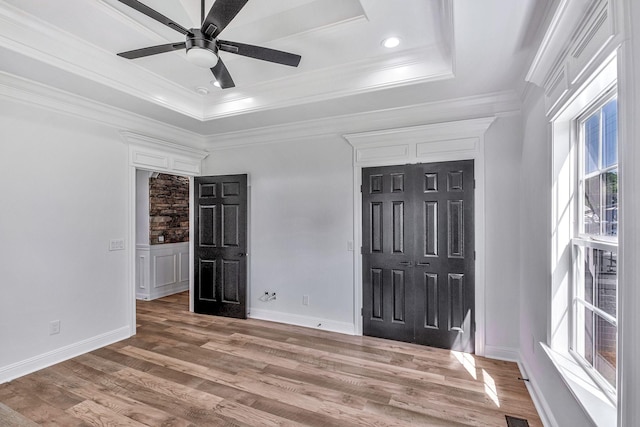 unfurnished bedroom with baseboards, a raised ceiling, light wood-style floors, and crown molding