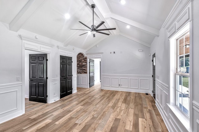 interior space featuring lofted ceiling with beams, light wood-style floors, a ceiling fan, and a decorative wall