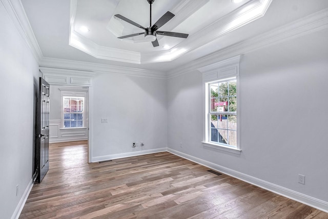 unfurnished room with a raised ceiling, wood finished floors, visible vents, and a wealth of natural light