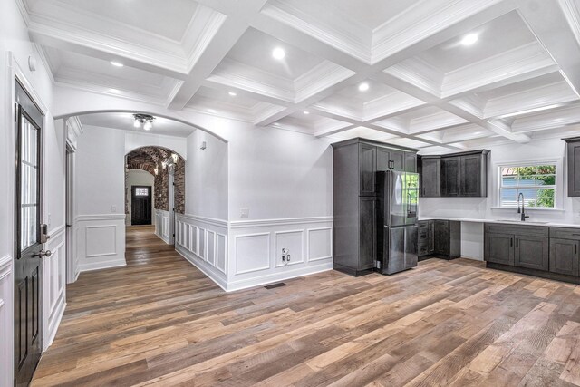 kitchen featuring arched walkways, beamed ceiling, freestanding refrigerator, and a sink