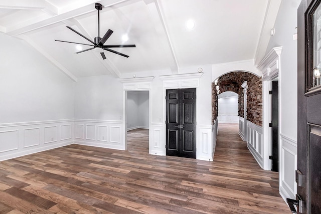 spare room featuring lofted ceiling with beams, arched walkways, dark wood-type flooring, and a ceiling fan