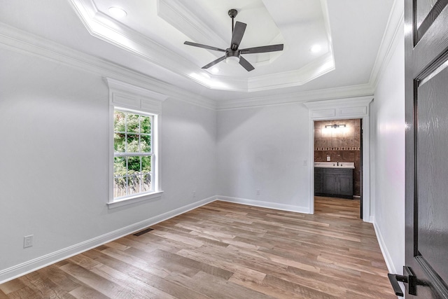 spare room with visible vents, light wood-style flooring, a ceiling fan, a tray ceiling, and crown molding