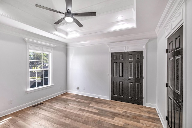 unfurnished bedroom featuring a tray ceiling, crown molding, baseboards, and light wood finished floors