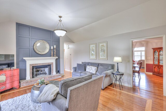 living room featuring light wood-type flooring, baseboards, lofted ceiling, and a fireplace