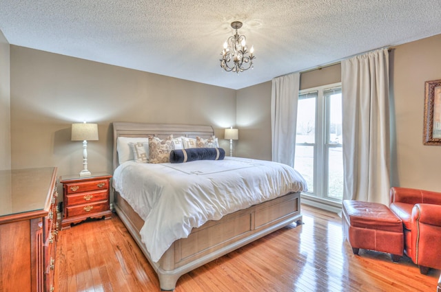 bedroom with light wood-style floors, multiple windows, a notable chandelier, and a textured ceiling