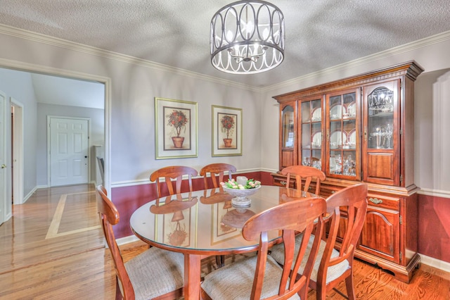 dining space featuring a textured ceiling, an inviting chandelier, crown molding, light wood finished floors, and baseboards