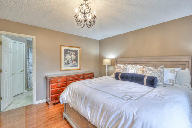 bedroom with light wood finished floors, baseboards, a textured ceiling, and an inviting chandelier