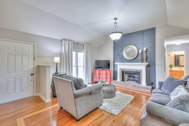 living room featuring light wood-type flooring, a brick fireplace, and vaulted ceiling