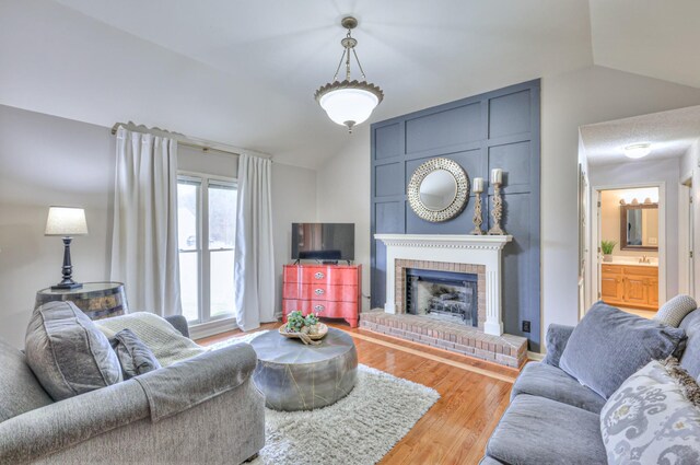 living area with lofted ceiling, a brick fireplace, and wood finished floors