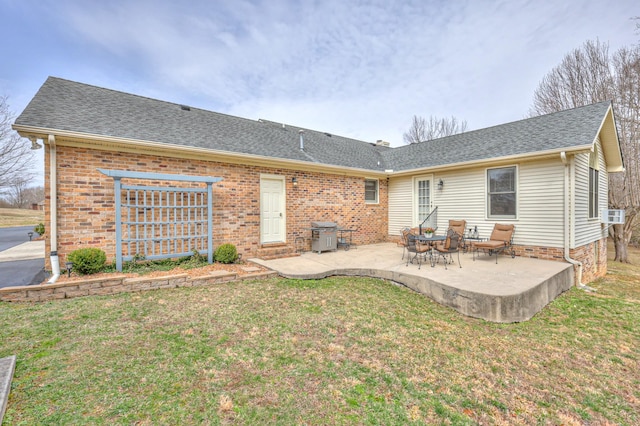 rear view of house with a patio area, a lawn, a shingled roof, and brick siding