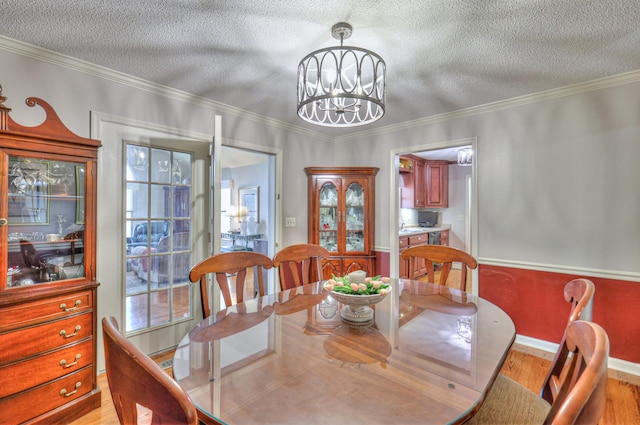 dining area with light wood-style flooring, a textured ceiling, an inviting chandelier, crown molding, and baseboards