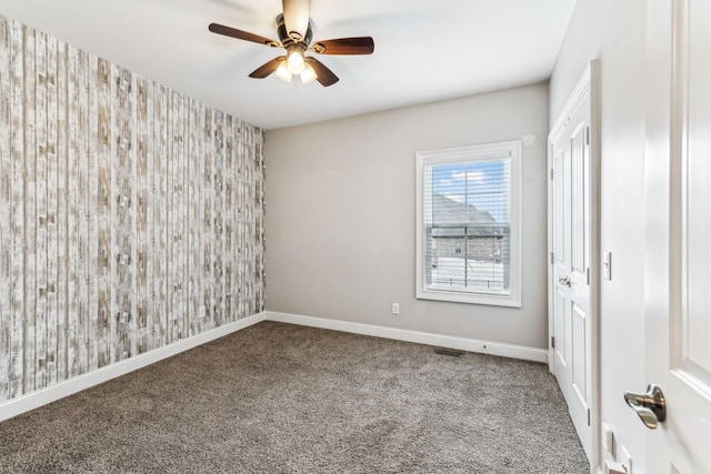 unfurnished room featuring a ceiling fan, carpet flooring, wallpapered walls, baseboards, and an accent wall