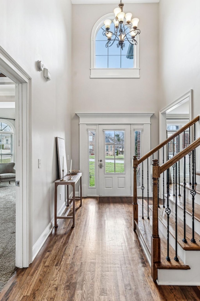 foyer featuring hardwood / wood-style floors, stairway, baseboards, an inviting chandelier, and a towering ceiling