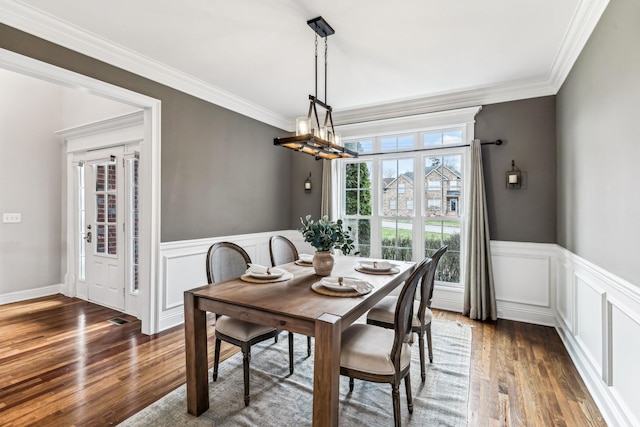 dining space with dark wood finished floors, a chandelier, wainscoting, and ornamental molding