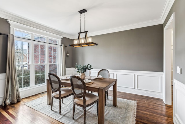 dining space with a wainscoted wall, crown molding, dark wood-style flooring, and an inviting chandelier