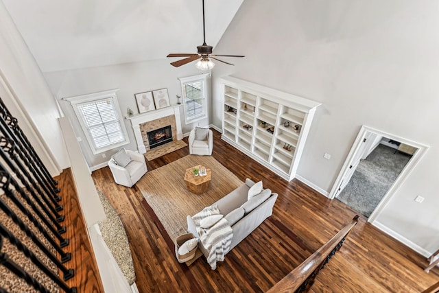 living area featuring stairs, wood finished floors, a warm lit fireplace, and high vaulted ceiling