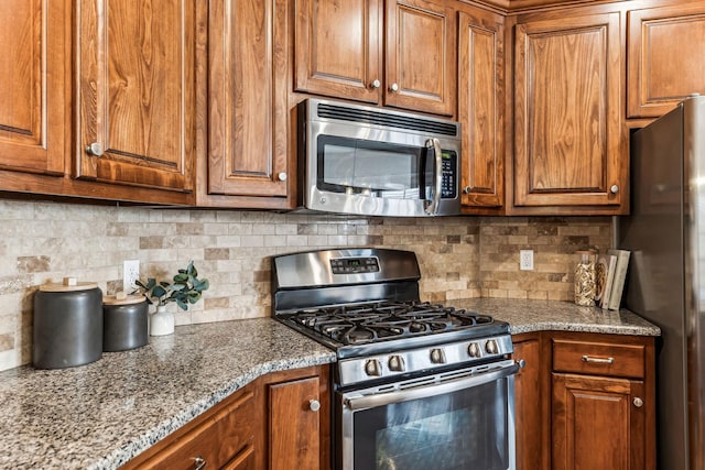 kitchen with decorative backsplash, brown cabinets, stainless steel appliances, and light stone countertops