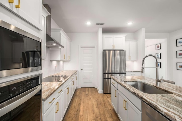 kitchen featuring visible vents, a sink, decorative backsplash, stainless steel appliances, and wall chimney range hood