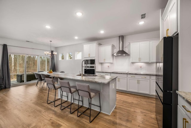 kitchen featuring visible vents, wall chimney range hood, a kitchen bar, appliances with stainless steel finishes, and a sink