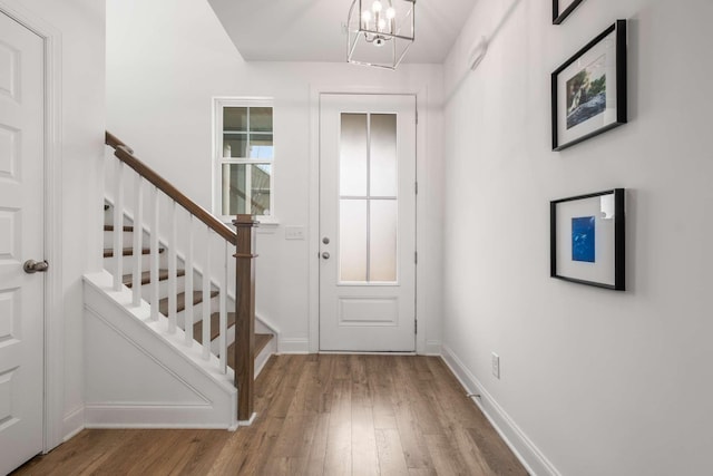 entryway featuring stairs, an inviting chandelier, wood finished floors, and baseboards