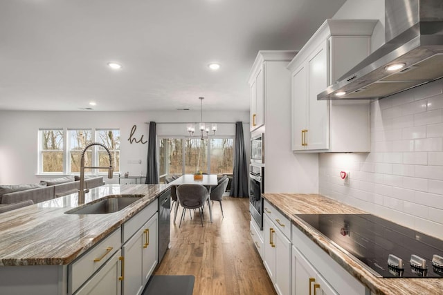 kitchen with light stone counters, a sink, appliances with stainless steel finishes, wall chimney range hood, and tasteful backsplash