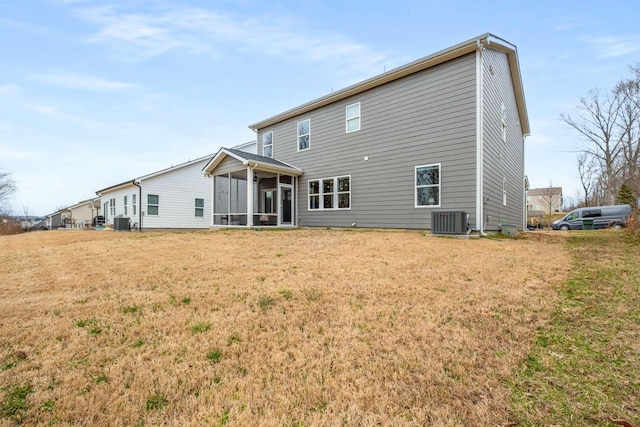 rear view of house with central AC unit, a lawn, and a sunroom