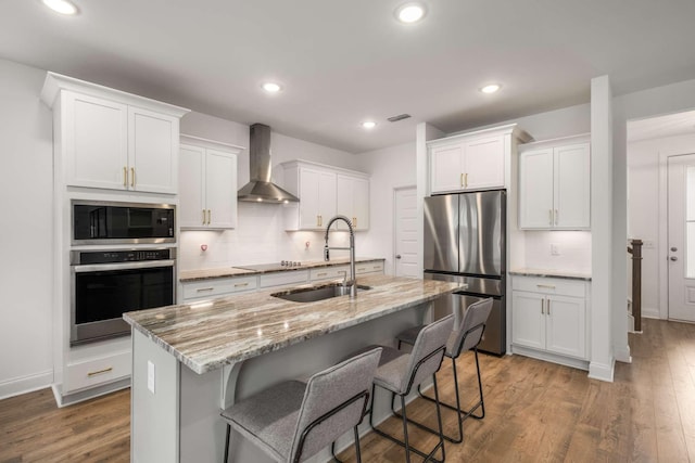 kitchen featuring wood finished floors, a sink, decorative backsplash, stainless steel appliances, and wall chimney exhaust hood