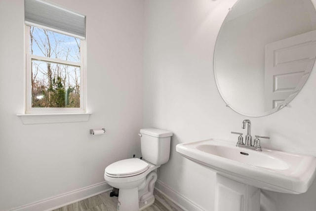 half bath featuring a sink, baseboards, toilet, and wood finished floors