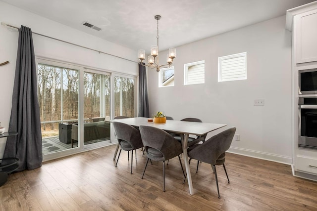 dining space with a notable chandelier, wood finished floors, visible vents, and baseboards