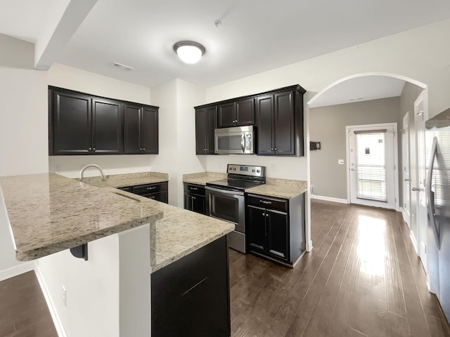 kitchen with light stone countertops, visible vents, a peninsula, dark wood-style flooring, and appliances with stainless steel finishes