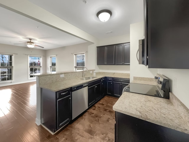 kitchen featuring a sink, open floor plan, appliances with stainless steel finishes, a peninsula, and dark wood-style flooring