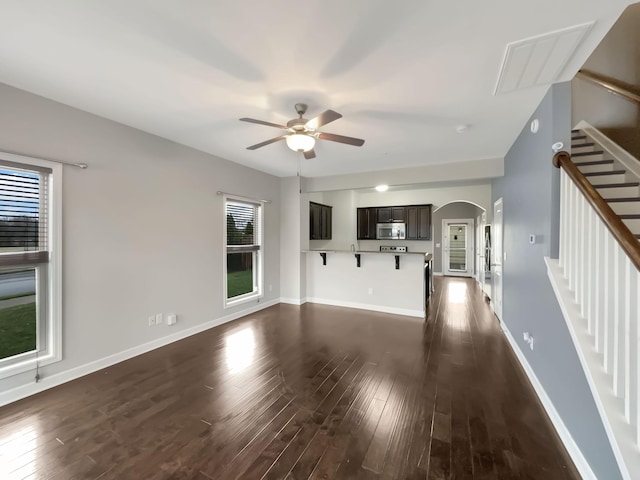 unfurnished living room with arched walkways, stairway, baseboards, and dark wood-style flooring