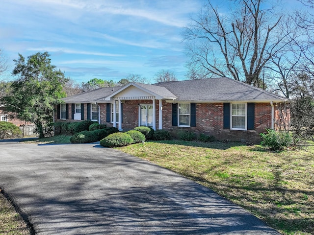 ranch-style home with brick siding, a front yard, and a shingled roof