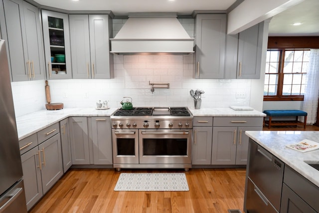 kitchen with stainless steel appliances, light wood-style floors, gray cabinetry, and custom range hood