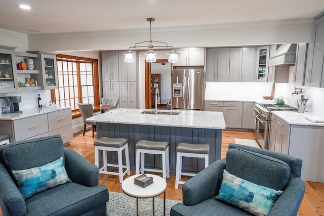 kitchen featuring a breakfast bar, gray cabinets, stainless steel appliances, wall chimney range hood, and decorative backsplash