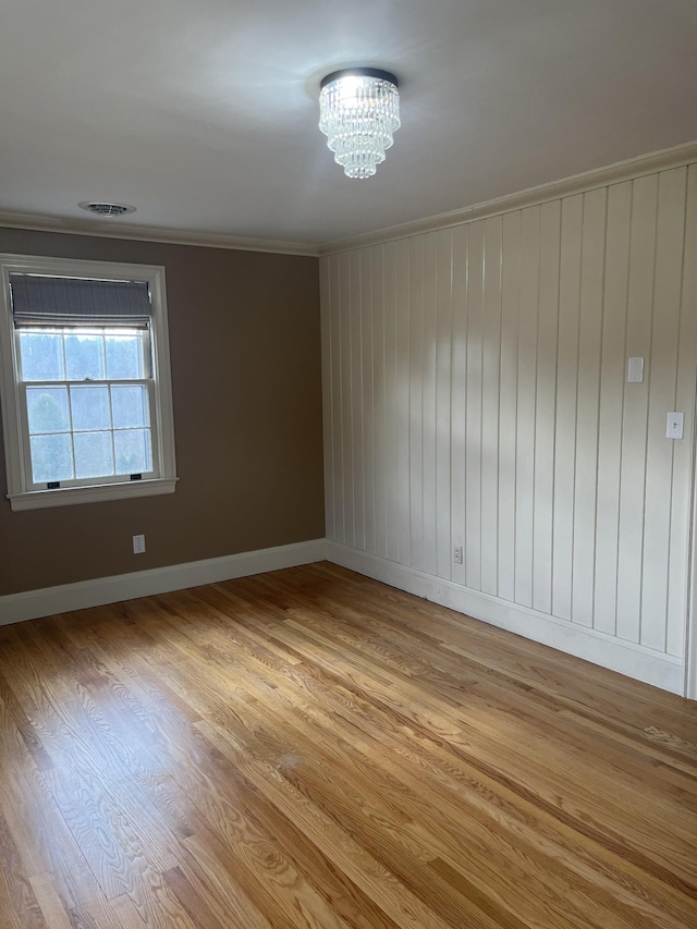 spare room with visible vents, ornamental molding, light wood finished floors, baseboards, and a chandelier