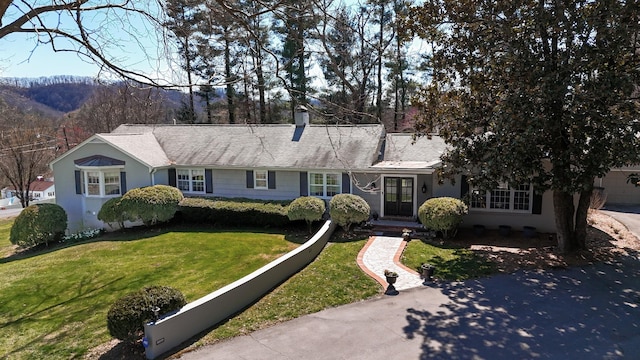 view of front facade with a front yard, roof with shingles, driveway, and a chimney