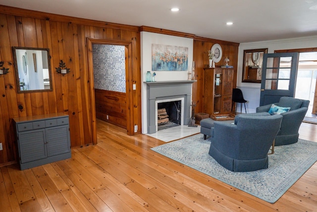 living room featuring wooden walls, crown molding, a fireplace with flush hearth, recessed lighting, and light wood-style flooring