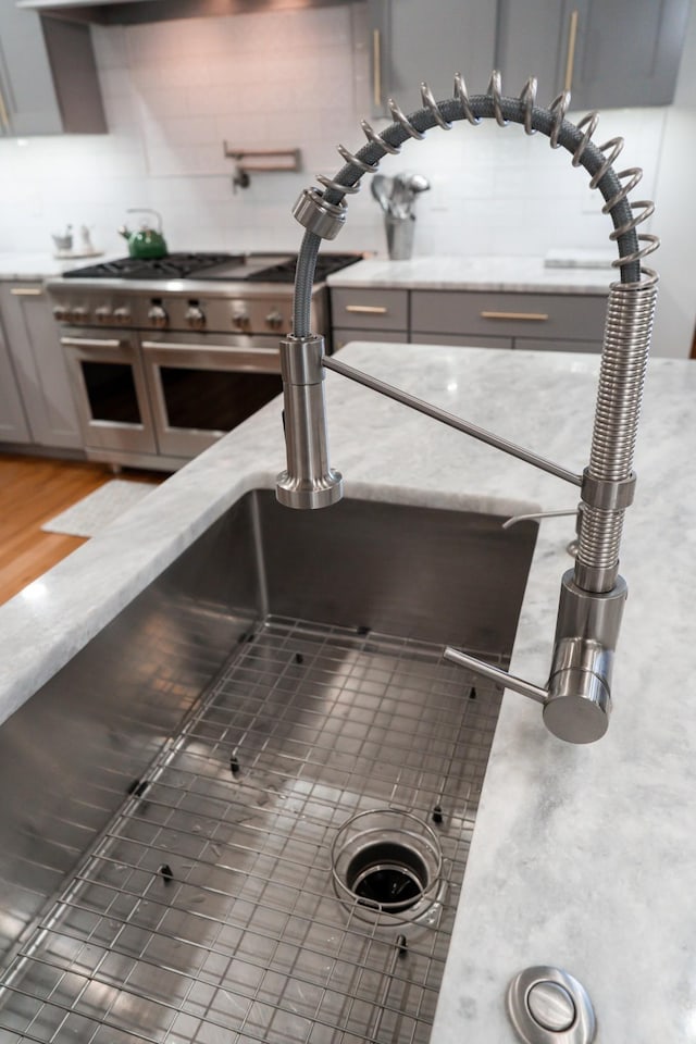 room details featuring range with two ovens, light stone counters, backsplash, and gray cabinets